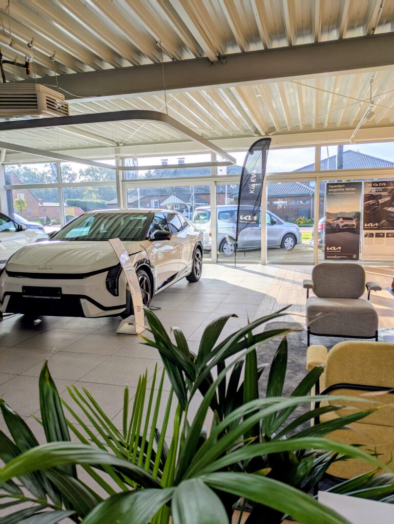 KIA-Ausstellungshalle mit modernem Elektroauto, hellen Sitzbereichen und großen Glasfronten.