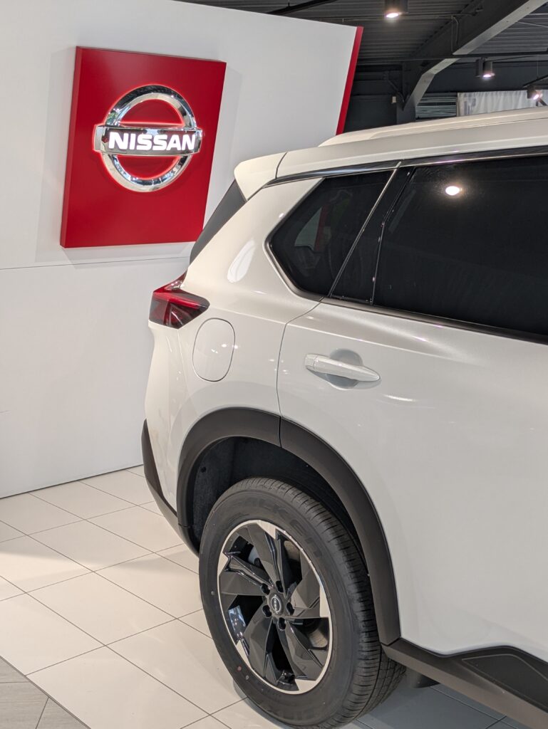 Weißes Nissan-Fahrzeug im Showroom vor einer Wand mit beleuchtetem Nissan-Logo.